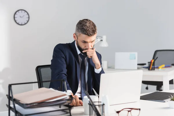 Thoughtful Businessman Looking Laptop Stationery Papers Blurred Foreground Table — Stock Photo, Image