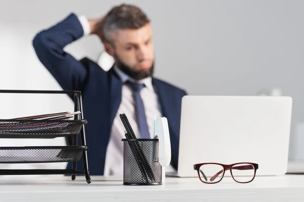 Brýle Papírnictví Stole Poblíž Zamyšleného Podnikatele Notebook Rozmazaném Pozadí — Stock fotografie