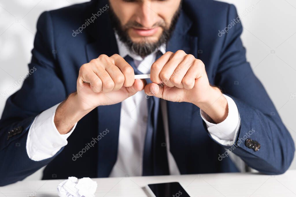 Cropped view of stressed businessman holding pencil near clumped paper and smartphone in office 