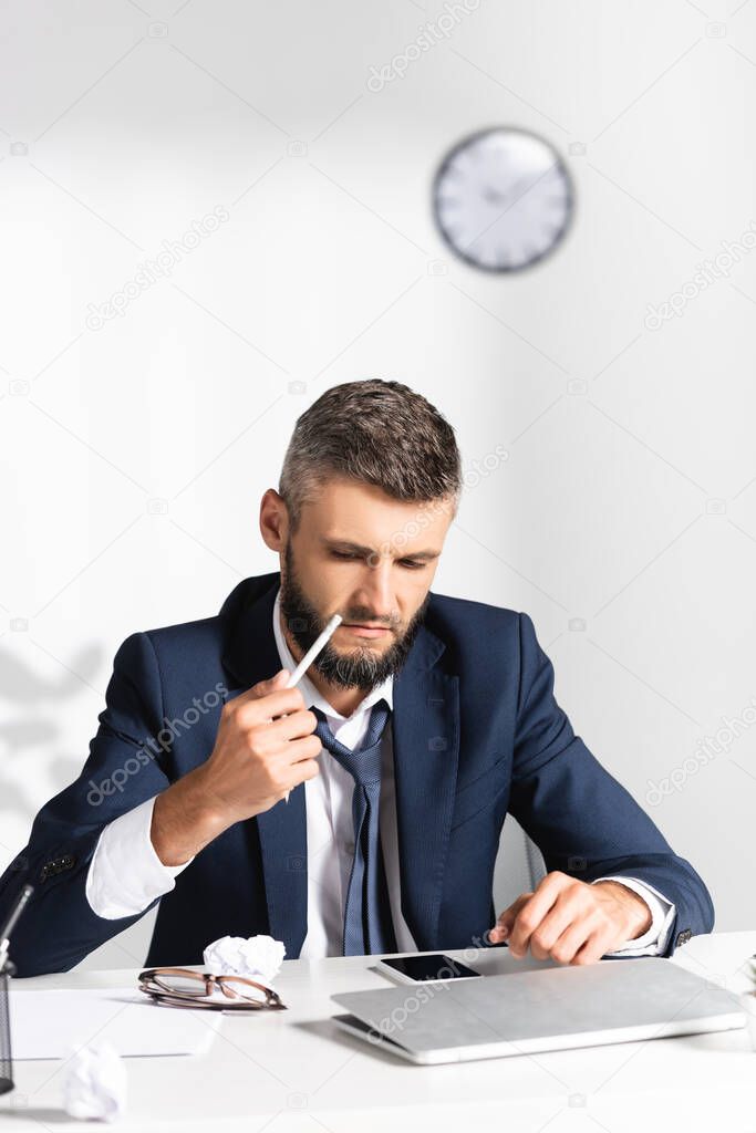 Businessman holding broken pencil near gadgets and clumped paper on blurred foreground 