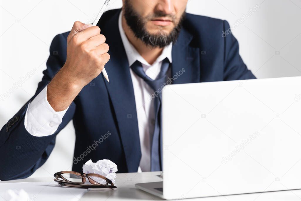 Cropped view of stressed businessman holding broken pencil near eyeglasses, laptop and clumped paper in office 
