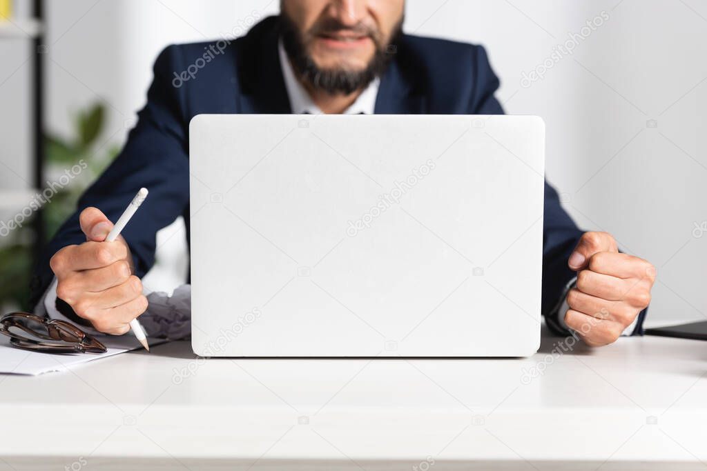 Cropped view of stressed businessman holding broken pencil near eyeglasses and laptop on office table 