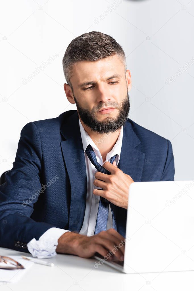 Businessman in formal wear feeling hot while using laptop on blurred foreground on working table 