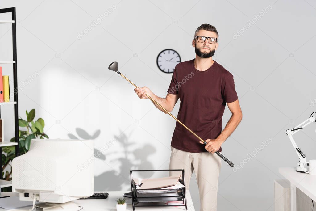 Businessman holding golf club near computer on blurred foreground in office 
