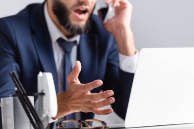 Bilgisayarın yanında akıllı telefondan konuşan işadamı görüşü ve bulanık önplanda gözlük. 