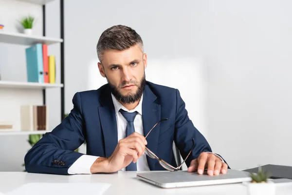 Empresario Sosteniendo Anteojos Mirando Cámara Cerca Computadora Portátil Primer Plano —  Fotos de Stock