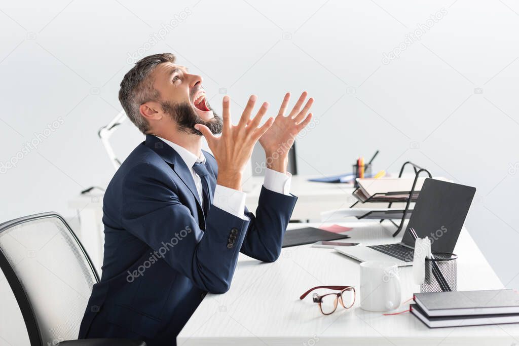 Irradiated businessman screaming while working near laptop and stationery in office 