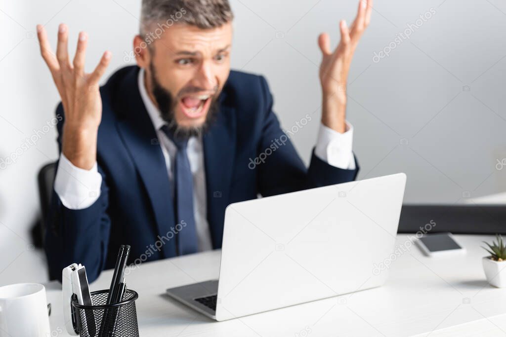 Stationery on table near screaming businessman and laptop on blurred background in office 