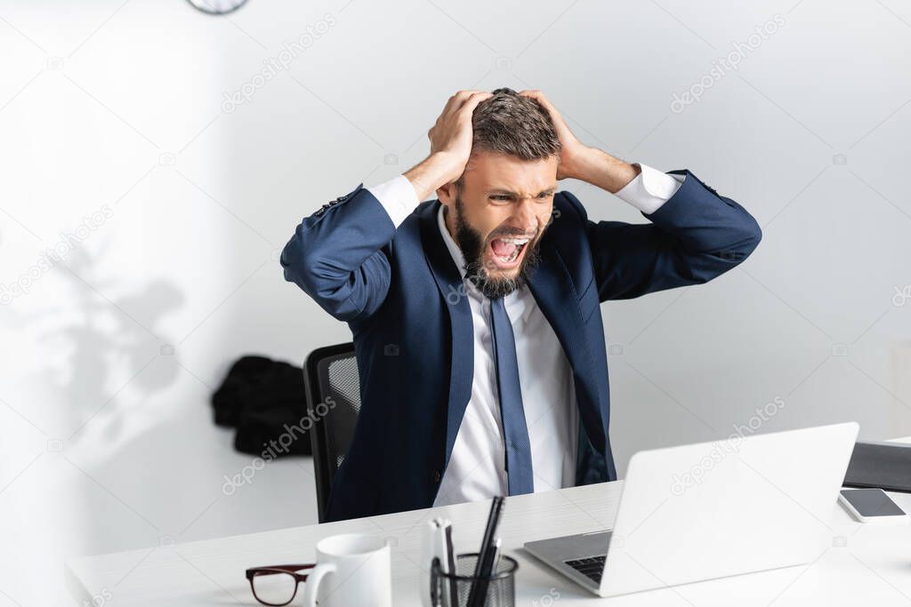 Businessman screaming and touching head during nervous breakdown in office 