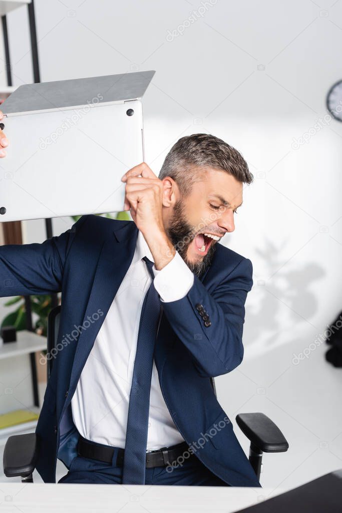 Screaming businessman holding laptop during nervous breakdown in office 
