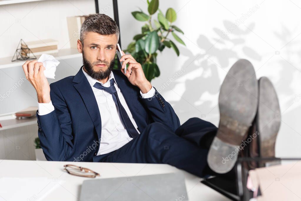Nervous businessman holing clumped paper while talking on smartphone while working in office 