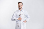 Vorderansicht des lächelnden Arztes mit erhobenem Daumen und Hand in Tasche, trägt weißen Mantel mit hängender Brille auf weißem Hintergrund