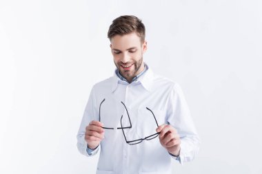 Gülümseyen doktor beyaz üzerine siyah çerçeveli gözlüklere bakıyor ve onları tutuyor.