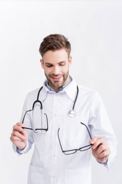 Gülümseyen doktor beyaz üzerine siyah çerçeveli gözlüklere bakıyor ve onları tutuyor.