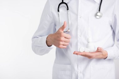 Baş parmağı havada, elinde lensler ve beyaz üzerine izole edilmiş plastik şişeyle göz doktorunun kırpılmış görüntüsü.