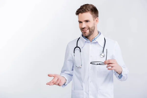 Smiling Young Adult Doctor Holding Eyeglasses Gesturing While Looking Away — Stock Photo, Image