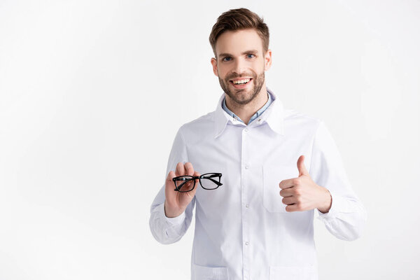 Вид спереди веселый офтальмолог с большим пальцем вверх, показывающий очки изолированные на белом