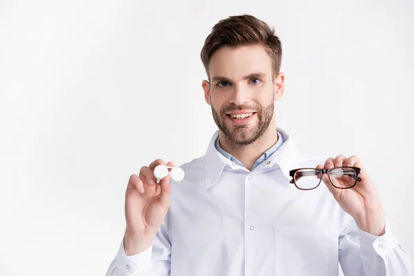 Front view of positive ophthalmologist with hands in air, showing eyeglasses and lenses container isolated on white