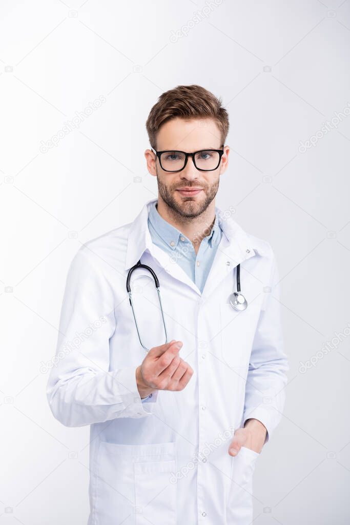 Positive ophthalmologist with hand in pocket wearing eyeglasses and looking at camera isolated on white