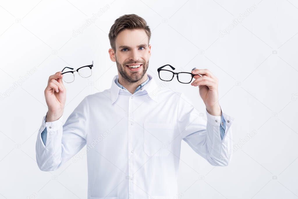 Front view of smiling ophthalmologist showing pair of eyeglasses, while looking at camera isolated on white