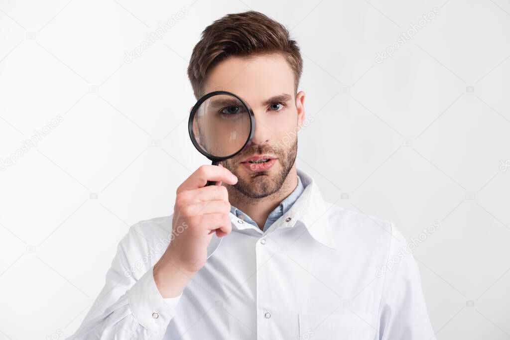 Portrait of confident ophthalmologist looking through loupe isolated on white