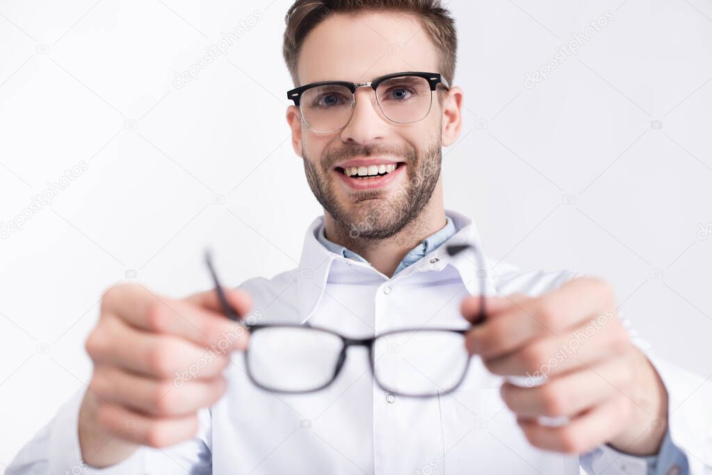 Smiling ophthalmologist putting eyeglasses isolated on white on blurred foreground