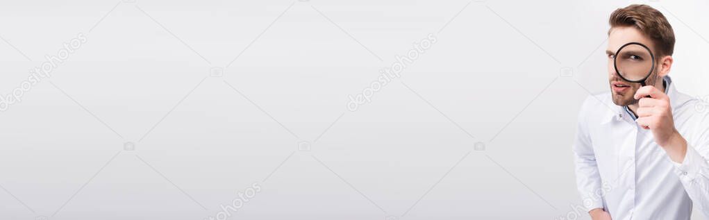 Curious ophthalmologist in white coat looking through magnifying glass on grey background, banner