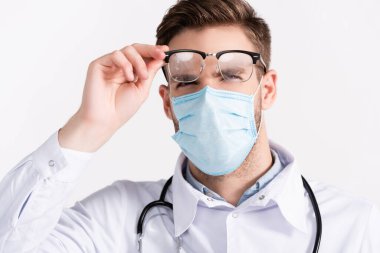 Tıbbi maskeli bir doktorun portresi buğulanmış gözlüklere bakıyor.