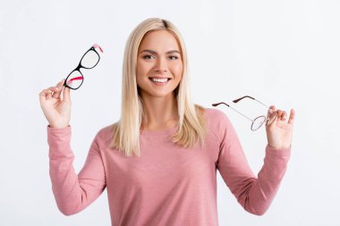 Positive woman looking at camera while holding eyeglasses isolated on grey clipart
