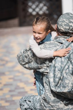 Back view of military man hugging smiling daughter on blurred background clipart