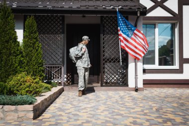 Military servicewoman with backpack leaving house, standing on threshold clipart