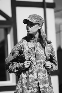 Confident military servicewoman looking away and holding backpack shoulder straps on blurred background, monochrome clipart
