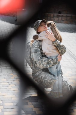 Daughter embracing mother in military uniform with blurred net on foreground, monochrome clipart