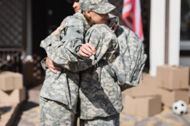 Military couple embracing and holding keys with blurred house and cardboard boxes on background clipart