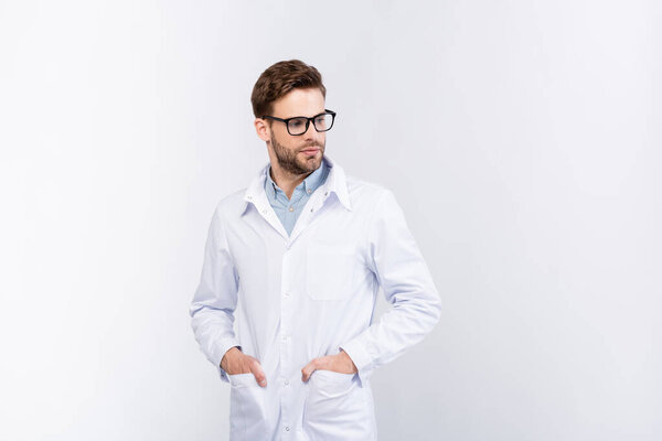 Ophthalmologist holding hands in pockets of white coat isolated on grey 