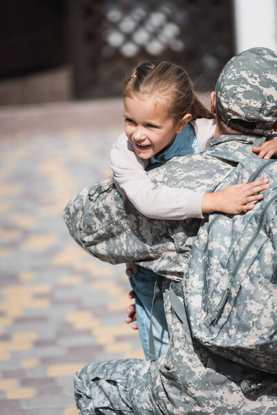Back view of military man hugging smiling daughter on blurred background