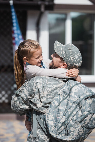 Happy father in military uniform hugging daughter on blurred background