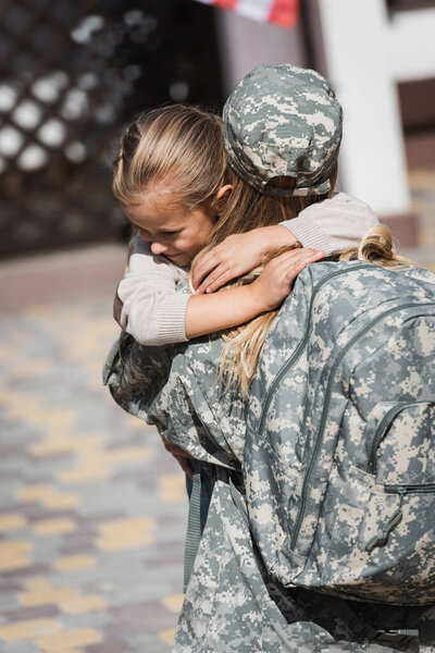 Smiling daughter hugging mother in military uniform on blurred background