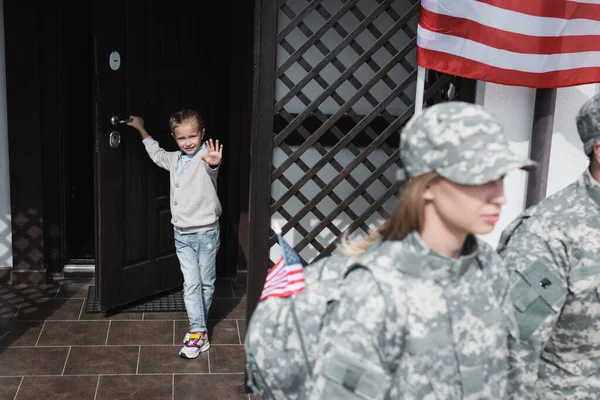 Smiling Daughter Waving Hand Standing Doorway American Flag Blurred Mother — Stock Photo, Image