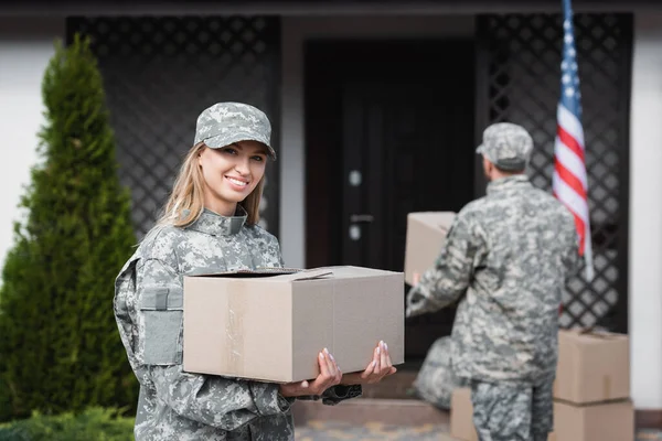 Smiling Woman Camouflage Holding Cardboard Box Looking Camera Blurred Military — Stock Photo, Image