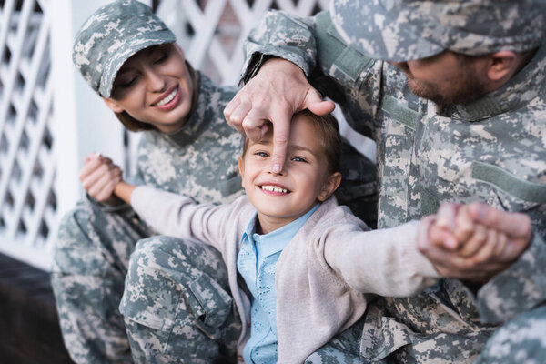 Cheerful military father and mother with daughter having fun while sitting on house threshold