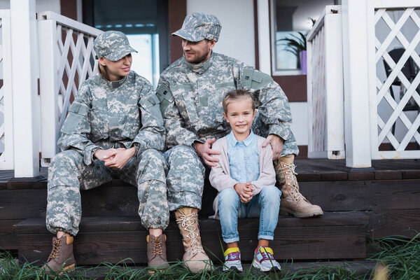 Smiling military father and mother with daughter sitting on house threshold