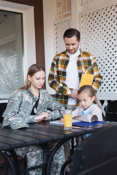 Chica Escribiendo Cuaderno Mientras Está Sentado Cerca Padre Madre Casa — Foto de Stock