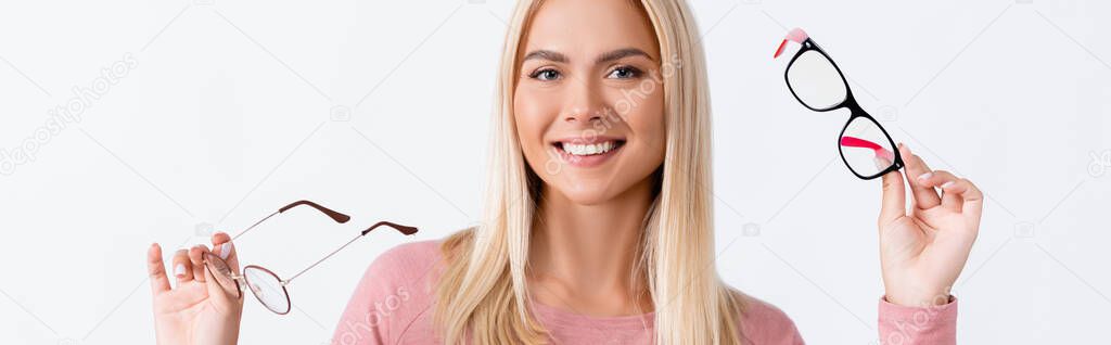 Happy blonde woman holding pair of eyeglasses, while looking at camera isolated on white, banner