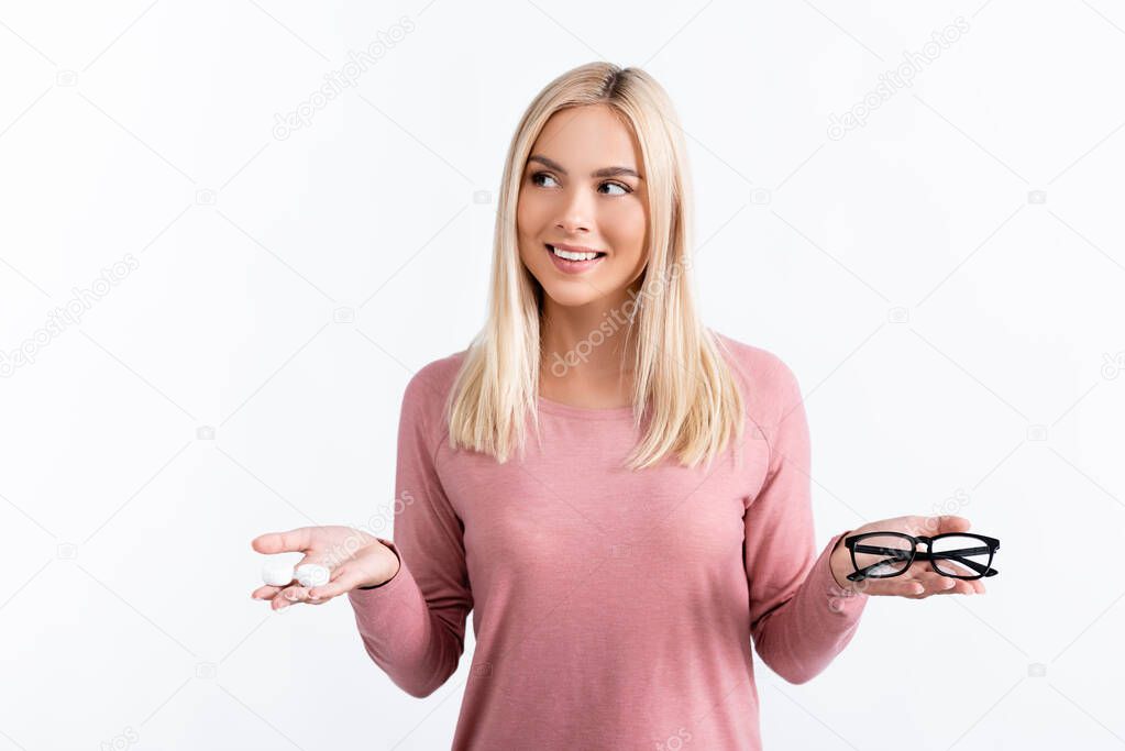 Positive woman looking away while holding box with contact lenses and eyeglasses isolated on white