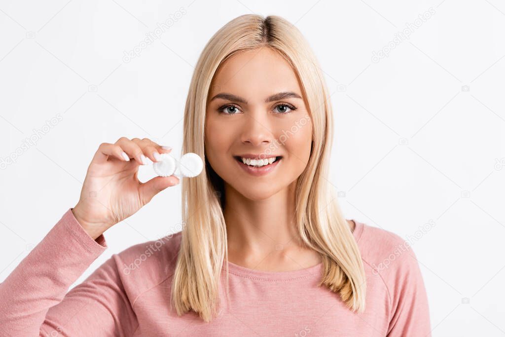 Smiling blonde woman holding container with contact lenses isolated on white