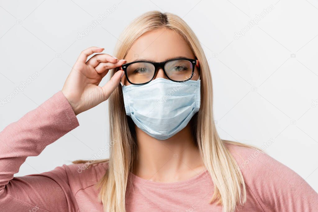 Young woman in medical mask and misted eyeglasses looking at camera isolated on grey