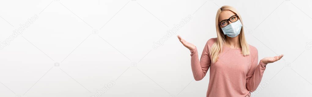 Confused woman in eyeglasses and medical mask showing shrug gesture isolated on grey, banner 