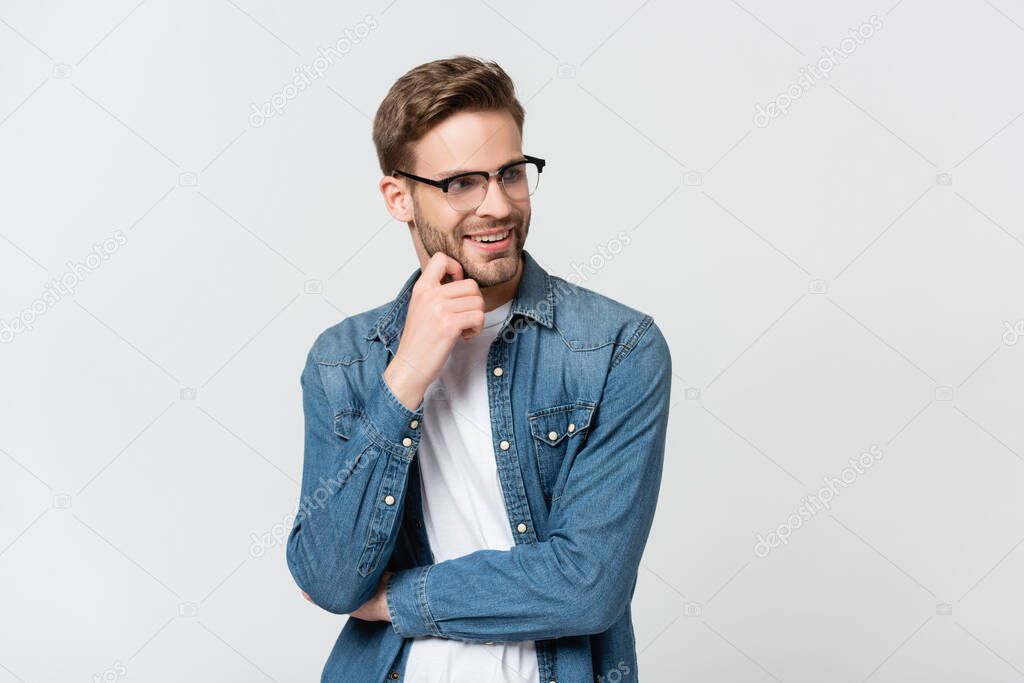 Young man in eyeglasses smiling while looking away isolated on grey