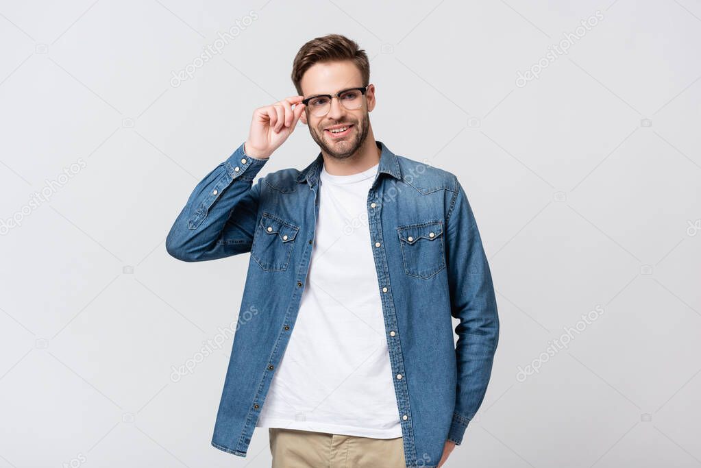 Smiling man touching eyeglasses isolated on grey